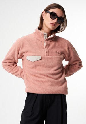 Hellrosa Fleece-Pullover mit hohem Kragen, knöpfbarer Leiste und kontrastierendem beigen Brusttasche. Weicher Stoff, lässige Passform.