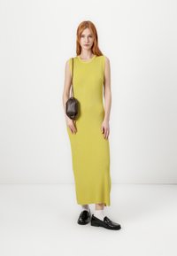 Dlhé, ribované šaty v jasne žltej farbe, so bezrukávovým dizajnom. V kombinácii s čiernymi mokasínami a malou hnedou crossbody taškou.