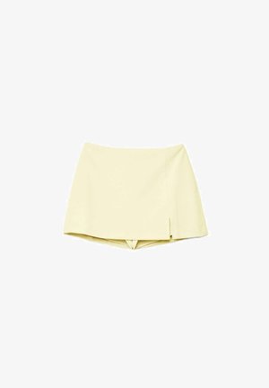 Minigonna gialla chiaro con una piccola spacco laterale, che combina la parte frontale della gonna con pantaloncini incorporati sotto, mostrata su sfondo bianco.