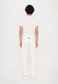 Jeans blancs ajustés et un t-shirt blanc à manches courtes. Les jeans présentent une étiquette au dos et deux poches arrière. Texture du tissu lisse.