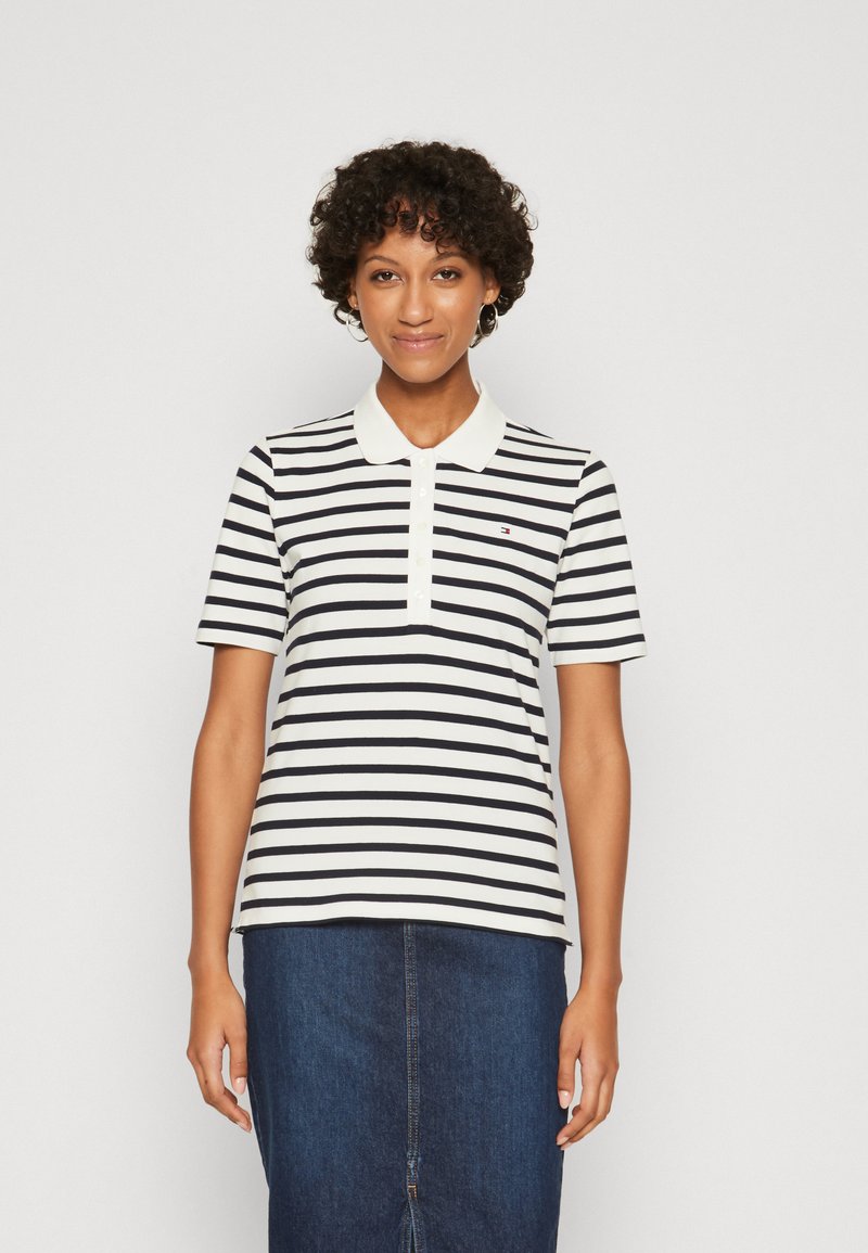Polo a righe nei colori navy e bianco, maniche corte e colletto classico. Presenta una chiusura con tre bottoni e un piccolo logo sul petto.