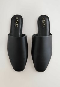 Juodi odiniai slip-on mules su smailiu pirštu, pasižymintys lygiu tekstūru ir minimalistiniu dizainu. Auksinis logotipas ant vidpadžio.