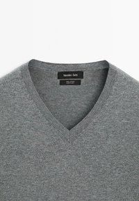Grauer V-Ausschnitt-Pullover aus 100% Baumwolle, mit einer weichen Textur, geripptem Kragen und dezenten Nähten entlang der Ränder.