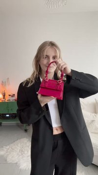 Petit sac à main rose brillant avec un design structuré, des poignées arrondies et des accents de quincaillerie dorée, présenté sur un fond neutre.