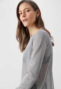 Langarmshirt in zilver, met een doorzichtige textuur en ronde halslijn. De stof heeft een subtiel, sprankelend patroon.