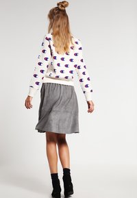 Sweatshirt crème avec motif de logo bleu et rouge, associé à une jupe grise. La tenue comprend des bottines noires et des détails en tissu texturé.