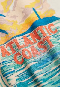 Tekst "ATLANTIC COAST" boven gestileerde oceaangolven met een zonsondergang en de silhouet van een gebouw of toren op de achtergrond, op stof.