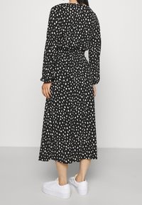 Musta mekko valkoisilla pilkuilla, keskipituinen, pitkät hihat, vyötärö tiukka, virtaava kangas. Yhdistetty valkoisiin tennareihin.