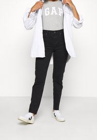 Černé džíny s vysokým pasem, šedé tričko s logem "GAP", bílá košile na knoflíky a bílé tenisky s černými akcenty.