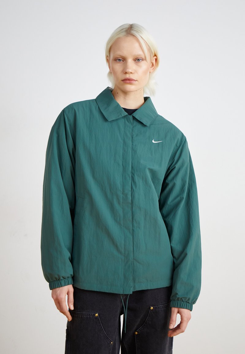 Zöld, könnyű dzseki klasszikus gallérral, rugalmas mandzsettákkal és diszkrét Nike logóval. Texturált anyagból készült, lazább szabással.