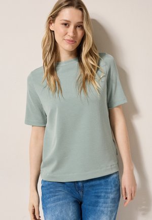T-shirt a righe verde chiaro con maniche corte, scollo rotondo e vestibilità comoda. Abbinato a jeans blu. Texture liscia. Design minimalista.