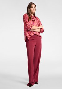 Rosa gemusterte Bluse mit Bindekragen, kombiniert mit bordeauxroten weit geschnittenen Hosen aus glattem Material, die maßgeschneiderte Akzente aufweisen.