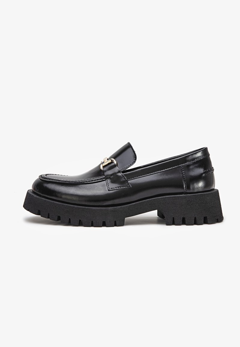 Mocassin en cuir noir avec semelle crantée épaisse et détail de boucle argentée sur le côté, présenté de profil sur fond blanc.