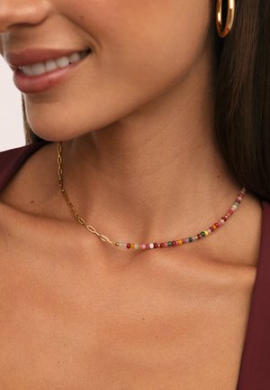 Collana in oro con una fila di piccole perle colorate in diverse sfumature, creando un design texturizzato e giocoso.