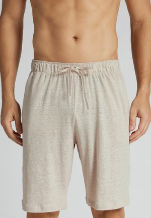 Bequeme beige Shorts mit elastischem Bund und gebundenem Kordelzug, getragen von einer oberkörperfreien Person vor grauem Hintergrund.