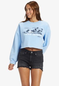 Sweatshirt accorciato blu chiaro con grafica "Dawn Patrol", che presenta palme nere e surfisti, abbinato a pantaloni shorts di denim neri.