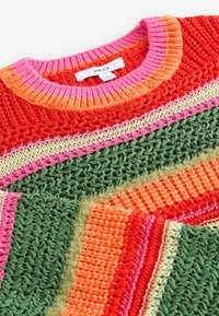 Stickad tröja med rund halsringning. Har livliga färger: röd, rosa, orange, grön och kräm. Texturerad mönster med varierande stygn.