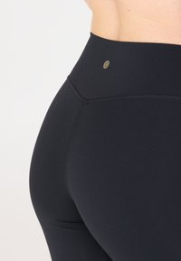Zwarte high-waisted leggings met een soepele textuur en subtiele logo-details bij de taille. Heeft versterkte naden en een aansluitend ontwerp.
