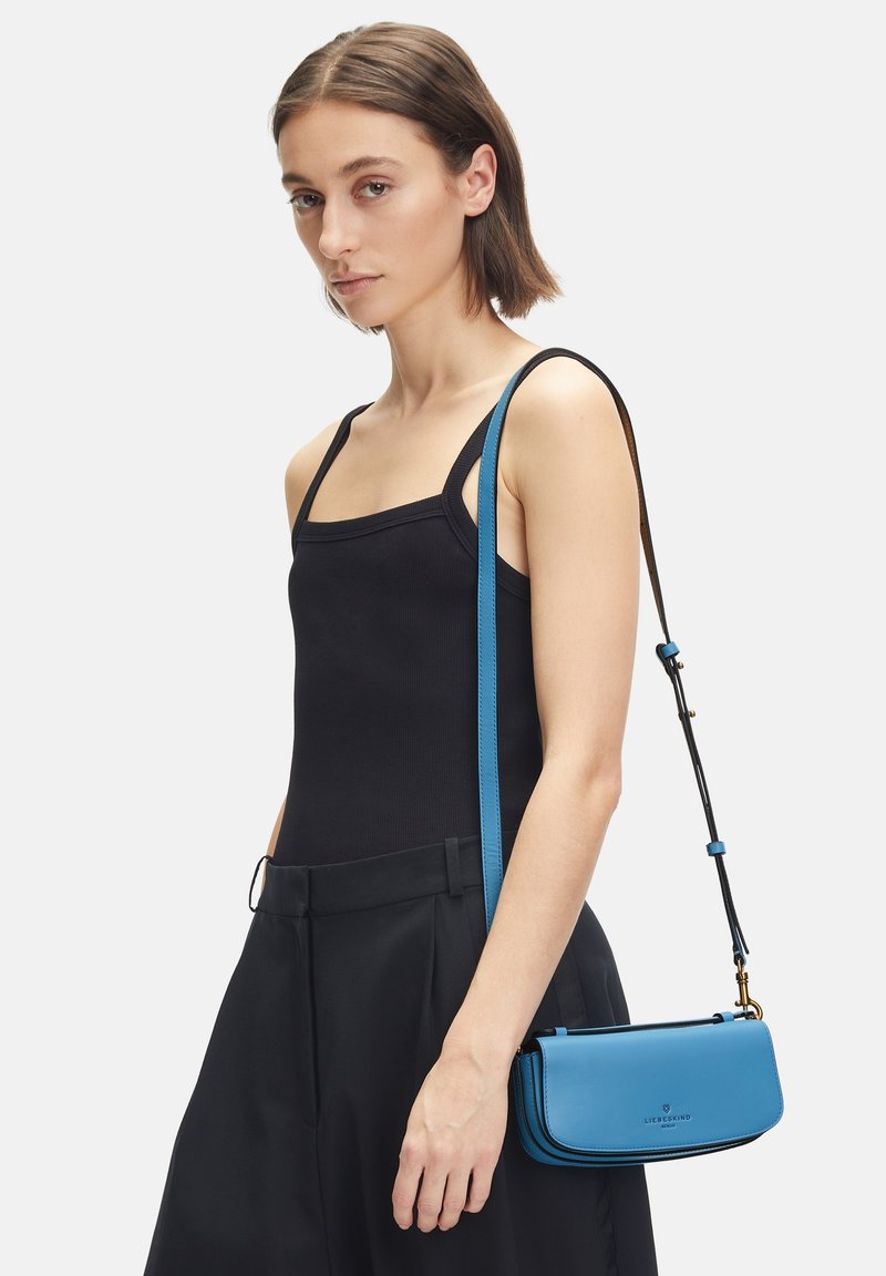 Niebieska skórzana torebka na ramię z czarnymi akcentami, prostokątny kształt i smukły regulowany pasek, z logo na przodzie.