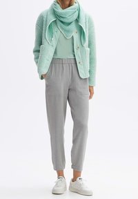 Veste polaire vert menthe avec boutons, portée sur un haut léger, associée à un pantalon gris fuselé et des baskets blanches. Tissu texturé, coupe décontractée.