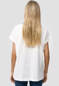 T-shirt bianco a maniche corte con una vestibilità rilassata e una texture morbida. Vista posteriore, con maniche arrotolate e orlo curvo.
