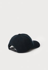 Black cotton baseball cap with a curved visor, adjustable strap at the back, and a subtle white logo on the side. Textured fabric.