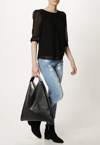 Svart blus med kort ärm och rynkad detalj vid halsringningen, kombinerad med ljusblå rivna jeans och en stor svart läderhandväska.