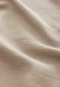 Tissu beige texturé avec de fines nervures et une surface lisse et extensible. La lumière se réfléchit doucement, mettant en valeur le motif subtil.