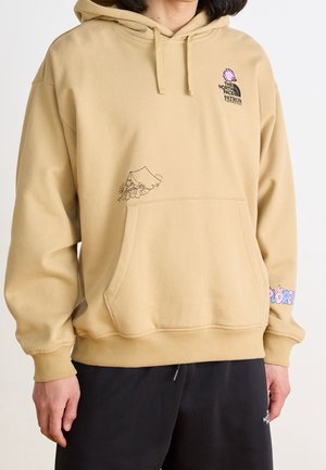 Sweat à capuche beige avec poche avant, petit graphique de tente de camping et fleur, logo "The North Face Patron" avec graphique rose sur la poitrine, texte coloré sur la manche.