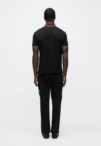 Svart polo med kontrasterende burgunderkrage og ermekant, kombinert med svarte jeans med rette ben. Ingen synlige grafikker eller mønstre.