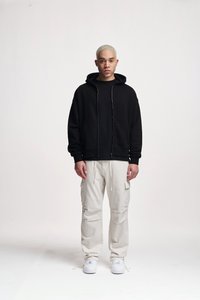 Felpa nera con zip, in cotone, vestibilità ampia. Abbinata a pantaloni cargo color avorio, con molteplici tasche, e sneakers bianche.