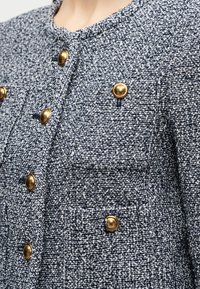 Ναυτικά μπλε και λευκό σακάκι από τουίντ με υφή υφάσματος, με στρογγυλά χρυσά κουμπιά μπροστά και στις τσέπες.