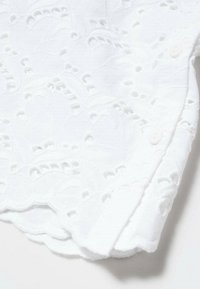 Tissu de coton blanc avec des motifs floraux brodés complexes, des bords en forme de festons et un petit détail de bouton près de l'ourlet.