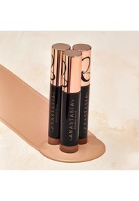 Drie cilindrische mascarabuisjes met roségouden doppen en zwarte bodems, bedrukt met het merk "Anastasia Beverly Hills", gelegen op een beige oppervlak.