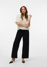 Haut en tricot crème à manches courtes avec une coupe ample, associé à un pantalon noir à jambes larges et des mules à talons marron avec des accents en dentelle.