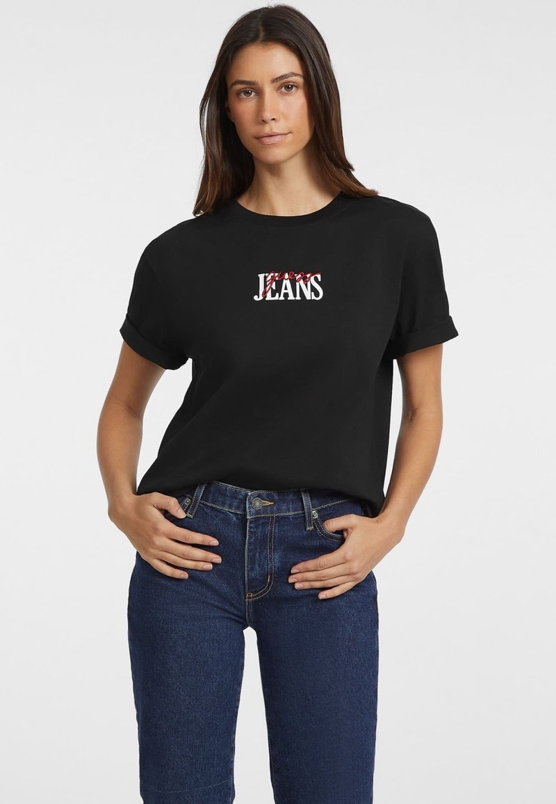 T-shirt nera con maniche arrotolate presenta una grafica bianca e rossa "Forever Jeans" sulla parte anteriore. Abbinata a jeans di denim blu scuro.