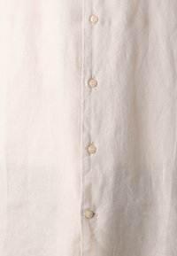 Light beige linen shirt with a button-up front featuring six beige buttons, a soft texture, and minimalistic design.