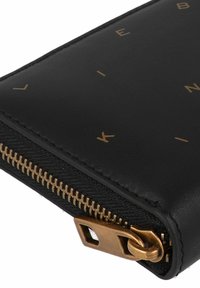 Portafoglio in pelle nera con scritte dorate, dotato di chiusura a zip con zip in metallo color oro, finitura testurizzata e design minimalista.