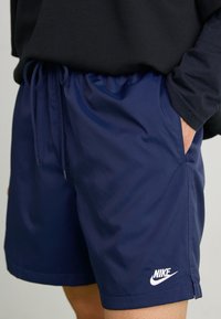 Navy Nike shorts made of lightweight material, featuring an elastic waistband, adjustable drawstring, and side pockets.