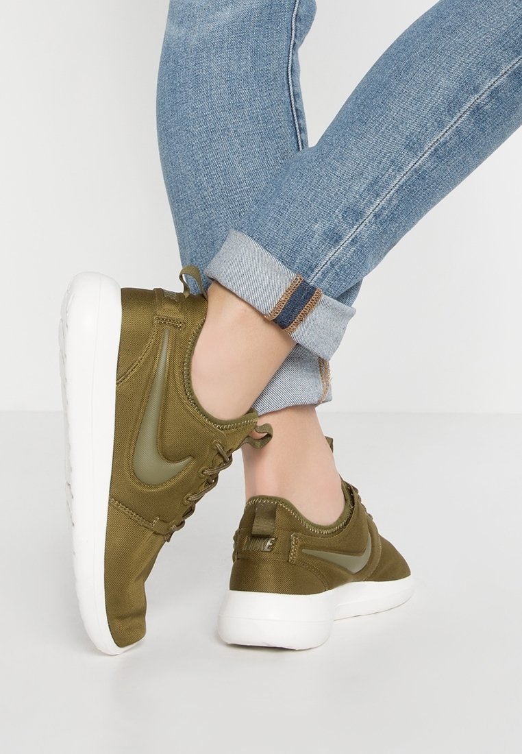 Olivgröna sportskor med slät tyg, vit sula och texturerade detaljer. Snörning och logotyp på sidan, tillsammans med uppvikt denim.