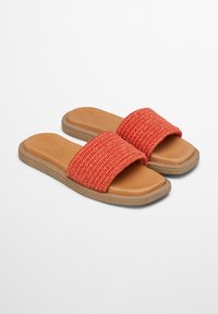 Woven coral slide sandals with a wide strap and tan cushioned footbed, featuring a flat, textured sole. Durable materials provide comfort.
