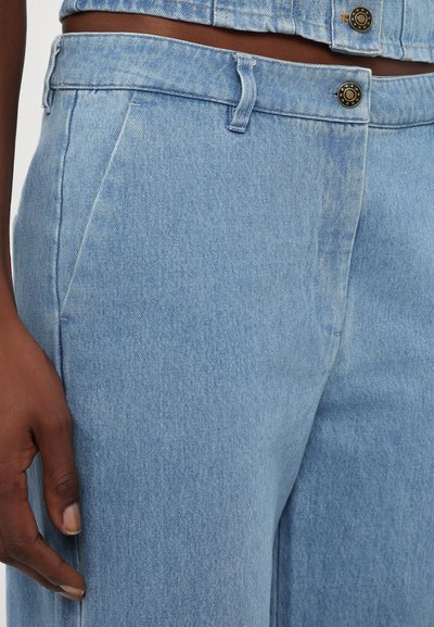 Lys blå denimbukser med rett snitt, frontlommer og knappelukking i midjen med en kontrastfarge knappedetalj.