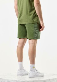 Oliven grønne shorts i en blanding av teksturerte og glatte stoffer, med en sidelomme, kombinert med hvite sneakers og sokker i cruiselengde.