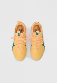 Zapatillas deportivas amarillas con acentos azules, material texturizado y cordones naranjas. Presenta un lazo en el talón y una suela plana para mayor estabilidad.