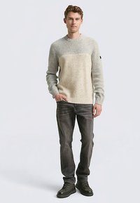 Maglione grigio chiaro a maglia con un blocco beige a contrasto, trama a costine, scollo rotondo; indossato con jeans scuri e sneakers nere.