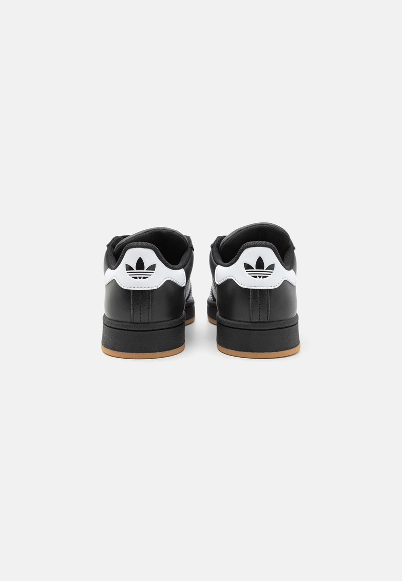 Zapatillas negras de cuero con un acabado texturizado, detalles en blanco en el talón y una suela de goma. Presentan el clásico detalle del logotipo de las tres franjas.