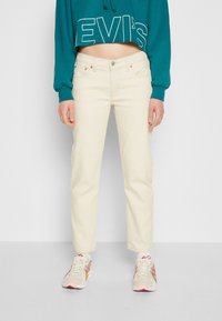 Geknipte teal hoodie met wit logo, beige rechte spijkerbroek en beige sneakers met rode accenten. Glad materiaal, losse pasvorm, casual ontwerp.