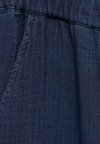 Denimska tkanina temno modre barve, z teksturirano tkano strukturo in vidnimi šivi. Material je mehak z rahlim sijajem in se na vrhu nabira.