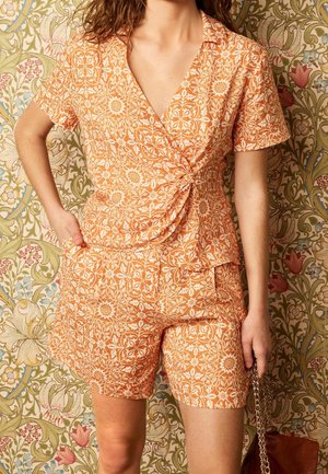 Kortærmet, indpakningsstil tøj i lys orange med et hvidt blomstermønster; har en knyttet detalje i taljen og matchende shorts.