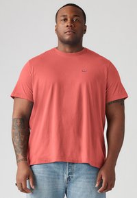 Kortærmet t-shirt med rund hals i koralfarvet bomuldsstof. Har et lille logo på brystet og en afslappet pasform. Bæres med lysvasket denim.